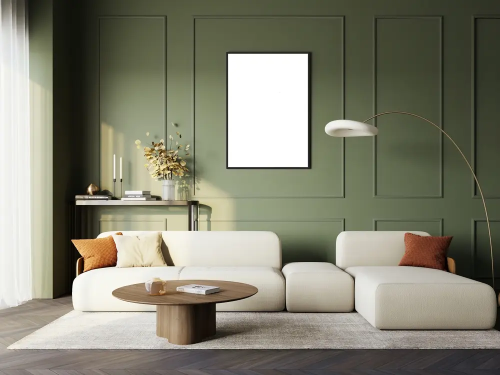 Salon moderne aux murs verts et à la corniche verticale épurée. Canapé d'angle blanc, table basse ronde en bois et lampadaire. Ambiance chaleureuse.