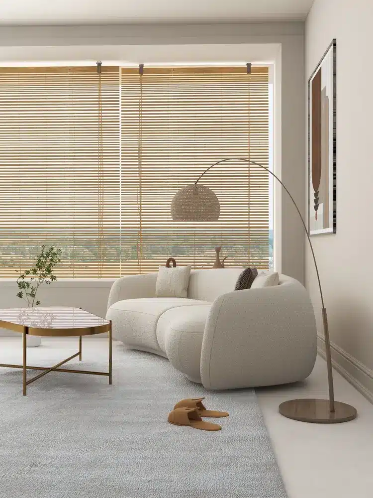 Un salon chaleureux avec un canapé crème, une table basse en bois et une grande fenêtre ornée de stores en bambou. Un lampadaire incurvé et des tableaux apportent une touche d'élégance.