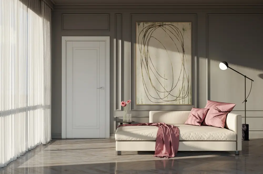 Un salon serein présente un canapé crème avec des coussins roses et un plaid drapé, des œuvres d'art modernes au mur, une douce lumière naturelle et des rideaux transparents qui expriment l'élégance.