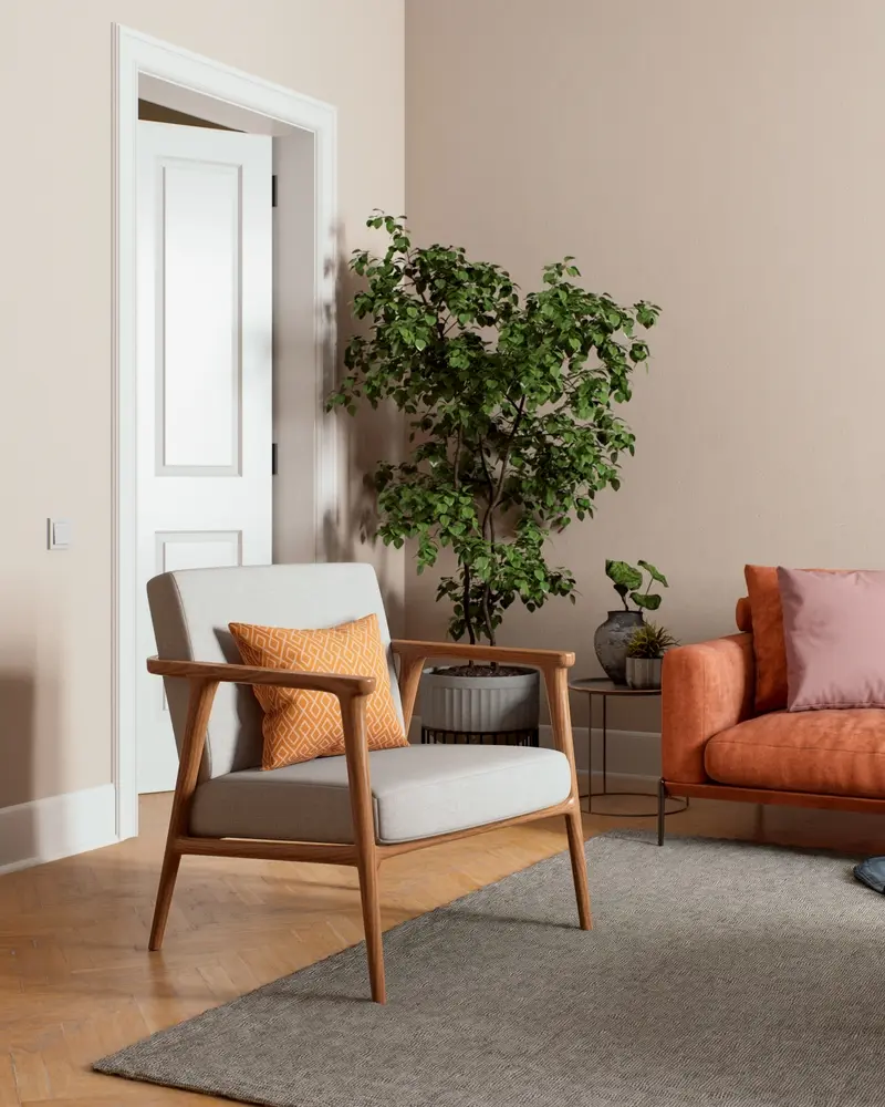 Salon moderne avec un fauteuil gris, un coussin orange, un canapé orange, un oreiller rose, une grande plante verte et une porte blanche ouverte. Ambiance chaleureuse et accueillante.