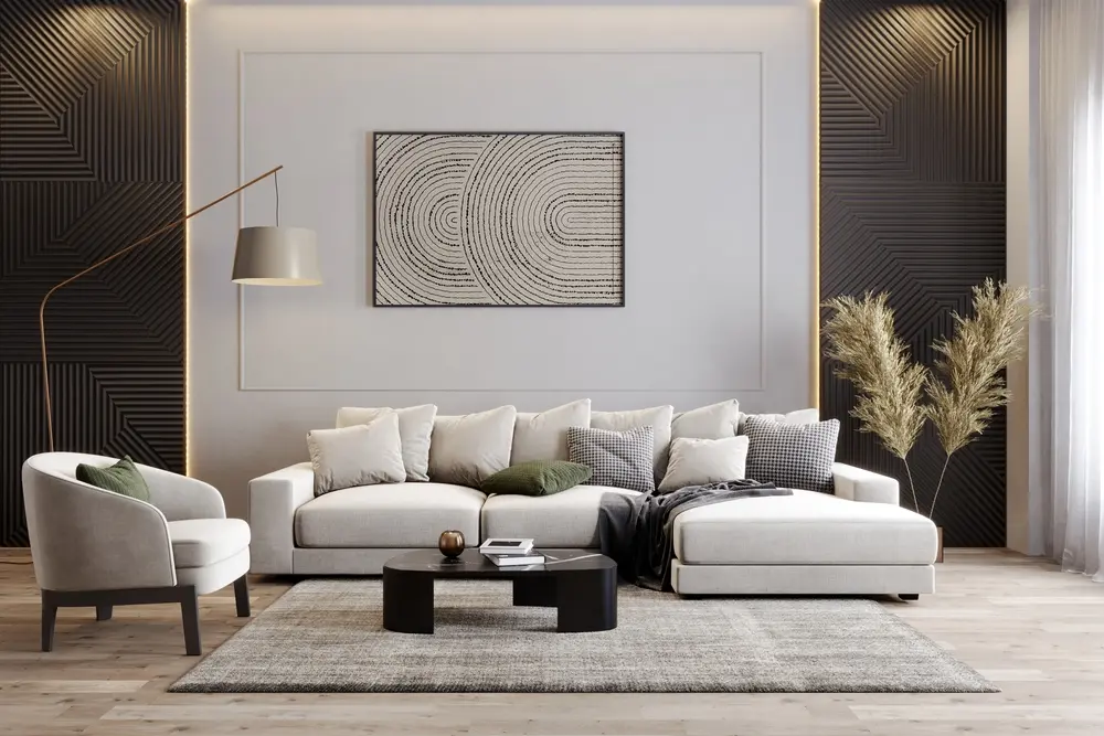Salon moderne avec un canapé d'angle beige, des coussins texturés et une table basse ronde noire. Une œuvre murale géométrique apporte une touche de contraste. Un éclairage chaleureux crée une ambiance cosy.