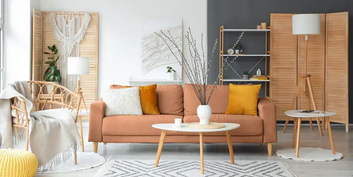 Un salon chaleureux avec un canapé beige, des coussins jaunes et un vase blanc sur une table basse ronde. Des tons neutres, un éclairage tamisé et une décoration moderne créent une atmosphère apaisante.