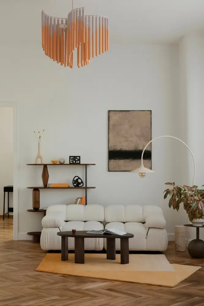 Un salon chaleureux avec un canapé crème, une table basse en bois et une grande fenêtre ornée de stores en bambou. Un lampadaire incurvé et des tableaux apportent une touche d'élégance. Un chat fait la sieste sur un tapis clair.