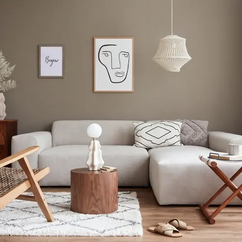 Salon contemporain avec canapé beige, tableau abstrait représentant un visage et suspension lumineuse en osier. Ambiance chaleureuse grâce aux touches de bois et aux motifs géométriques.