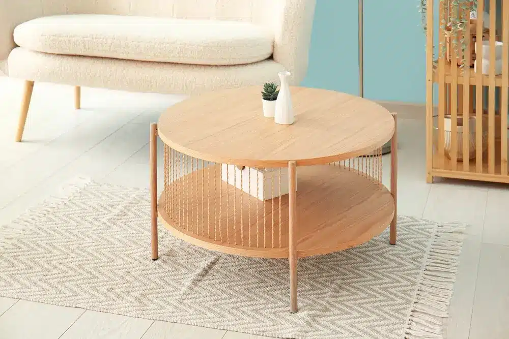 Une table basse ronde en bois, surmontée d'une petite plante et d'un vase, repose sur un tapis à motifs. Un canapé beige se dresse en arrière-plan, dans une pièce baignée d'une lumière tamisée.